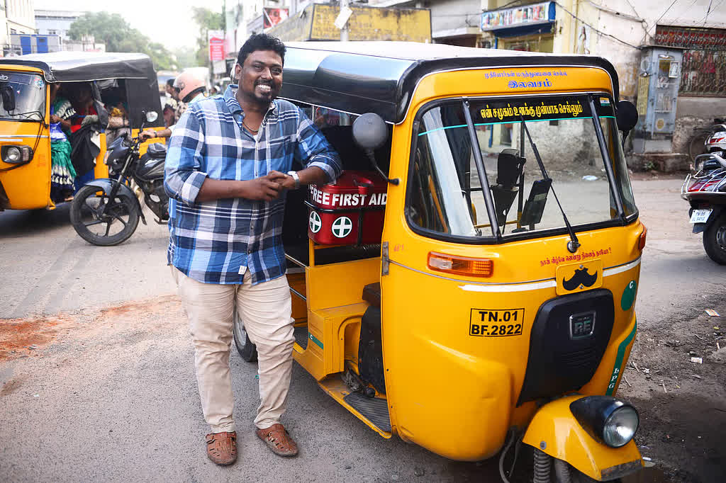 Founder D. Arul Raj smiling beside his yellow autorickshaw on a Chennai street, the auto carrying a free first-aid box